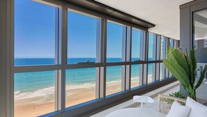 Een moderne kamer met grote ramen met uitzicht op een strand, een witte bank en een klein tafeltje.