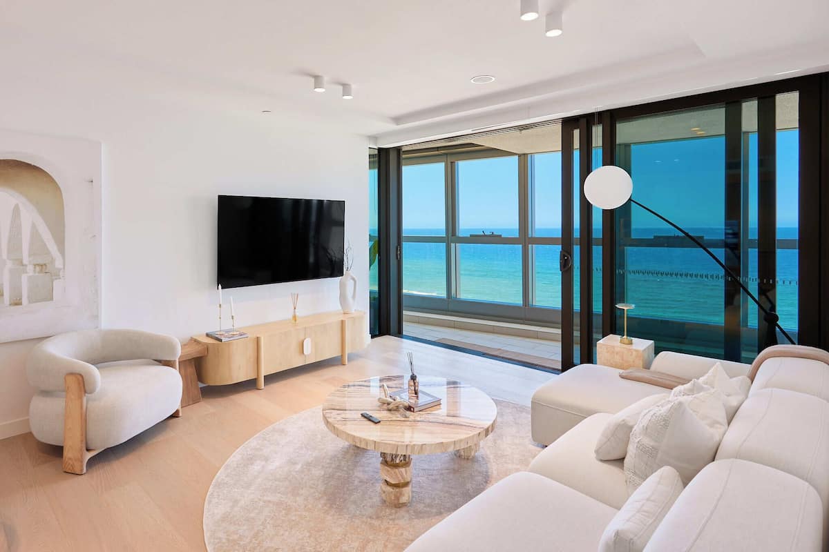 Una sala de estar moderna con un televisor grande, asientos cómodos y vistas al mar.