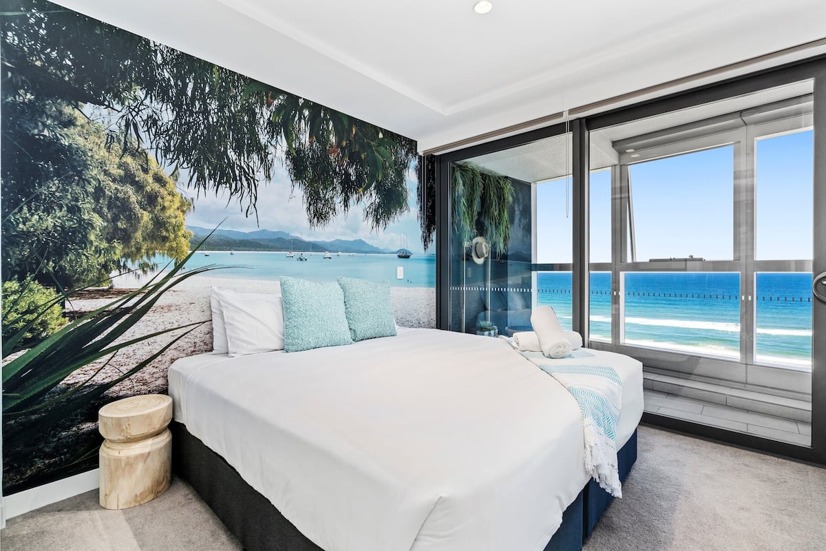Un dormitorio con una cama grande, vista al mar y un mural tropical.