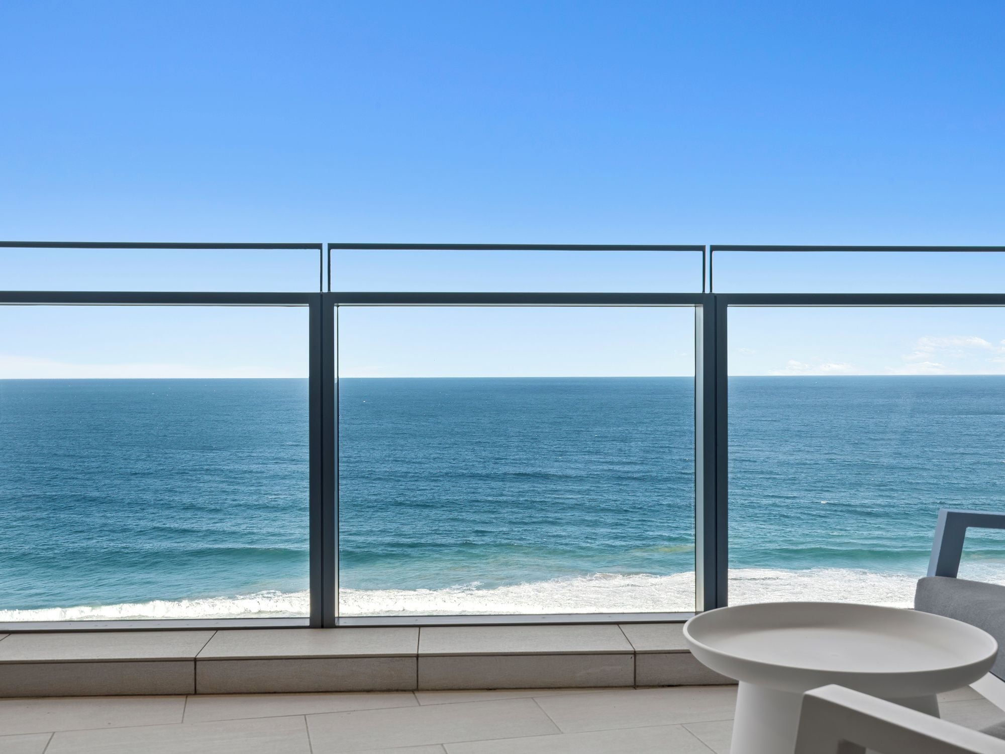 Un balcón con vistas despejadas al océano, una mesa blanca y una silla.