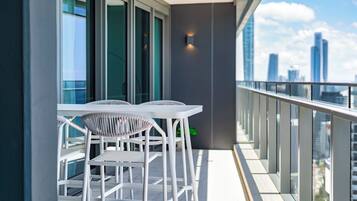 A balcony with white chairs and a table, overlooking a cityscape with tall buildings.