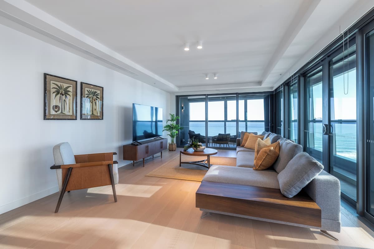 Una sala de estar moderna con sofá, televisión y un amplio ventanal con vista al océano.