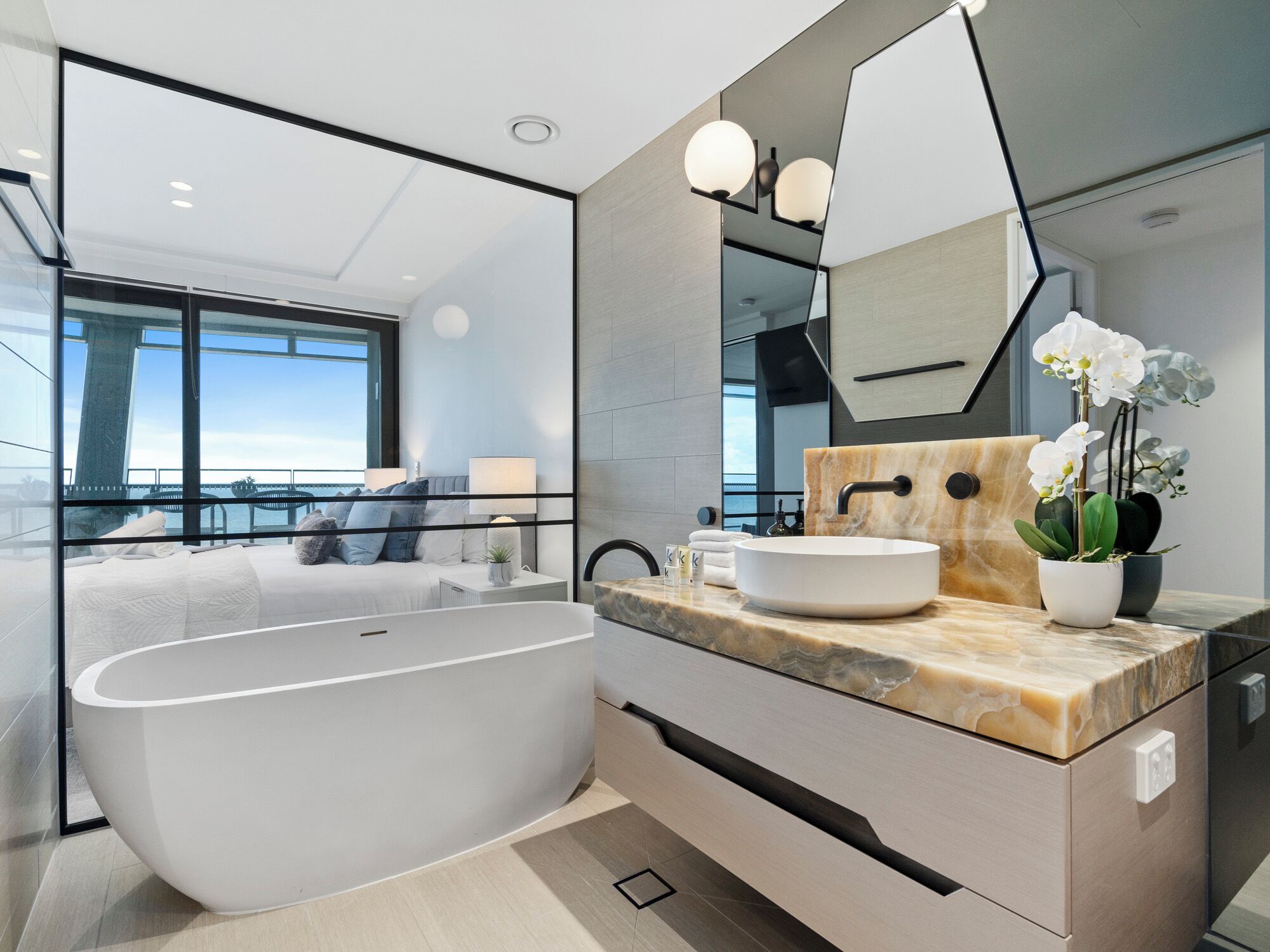 A modern bathroom with a freestanding bathtub, a marble countertop, and a large mirror.