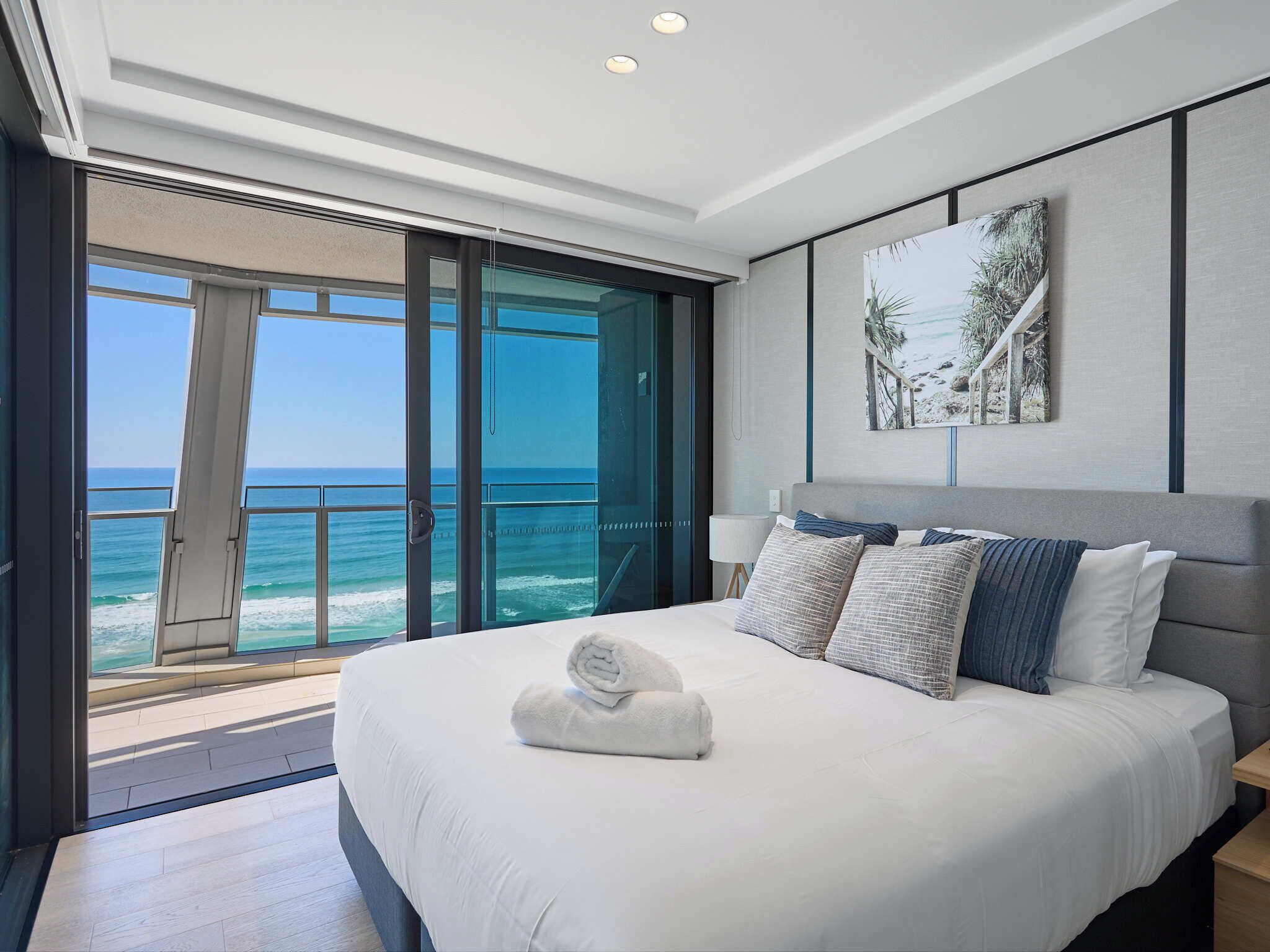 A modern hotel room with a large bed, a painting, and a view of the ocean.