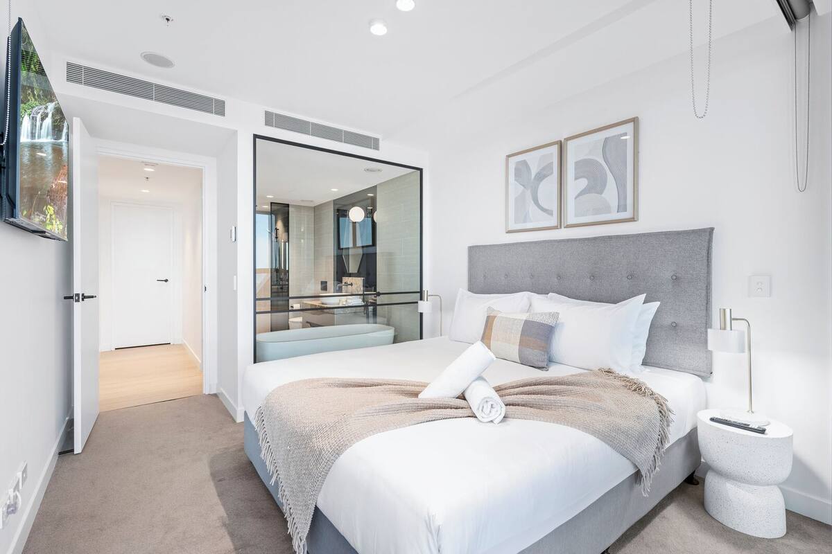 Un dormitorio moderno con una cama grande, un baño con paredes de vidrio y vista a una cascada.