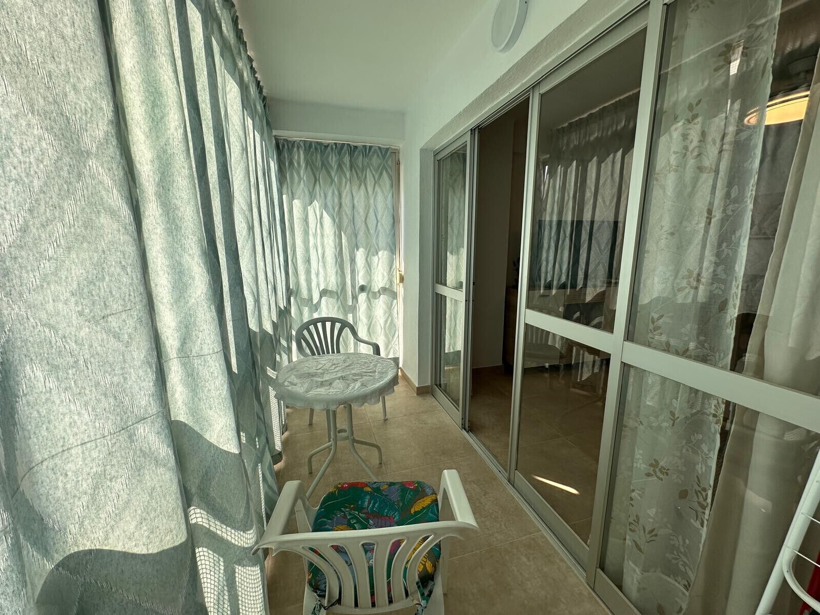 A balcony with a table and chairs, a sliding glass door, and a view of the outside.