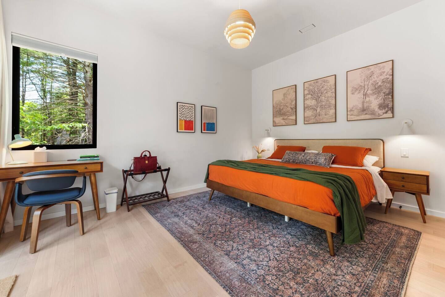 Ein Schlafzimmer mit Bett, Schreibtisch, Stuhl und einem Fenster mit Blick auf Bäume.
