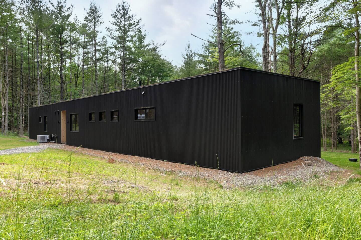 Une cabane moderne aux murs noirs et au toit plat, entourée d’une forêt.