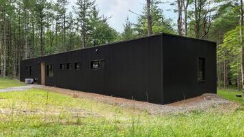 Une cabane moderne aux murs noirs et au toit plat, entourée d’une forêt.
