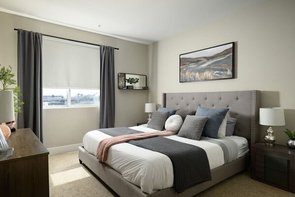 A modern bedroom with a large bed, grey curtains, a bedside table with a lamp, and a window with a view.