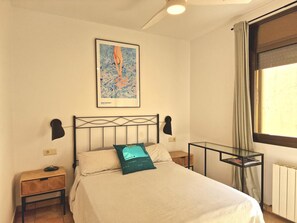 Une chambre à coucher comprenant un lit, une table de chevet, une commode, une œuvre d’art encadrée accrochée au mur, une fenêtre avec des rideaux et un radiateur.