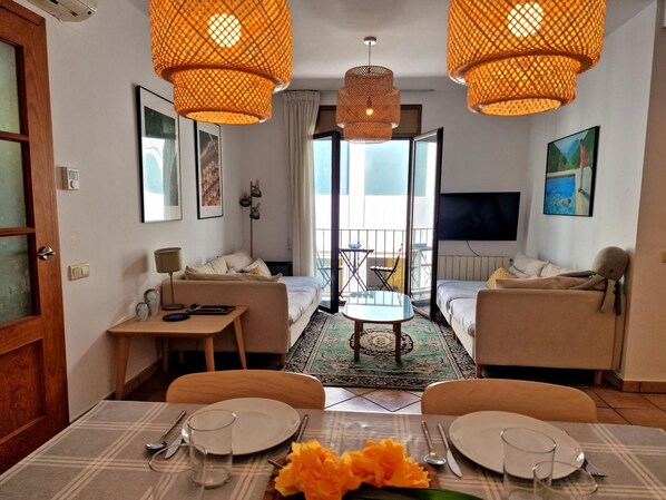 Un salon moderne avec un canapé, une table à manger pour deux personnes et un balcon offrant une vue agréable.