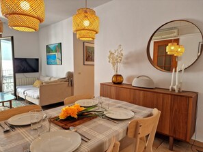 Un coin repas avec une table dressée pour quatre personnes, un canapé, un téléviseur et un miroir.