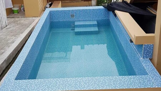 Una piscina rettangolare con bordo piastrellato, circondata da un solarium in cemento.
