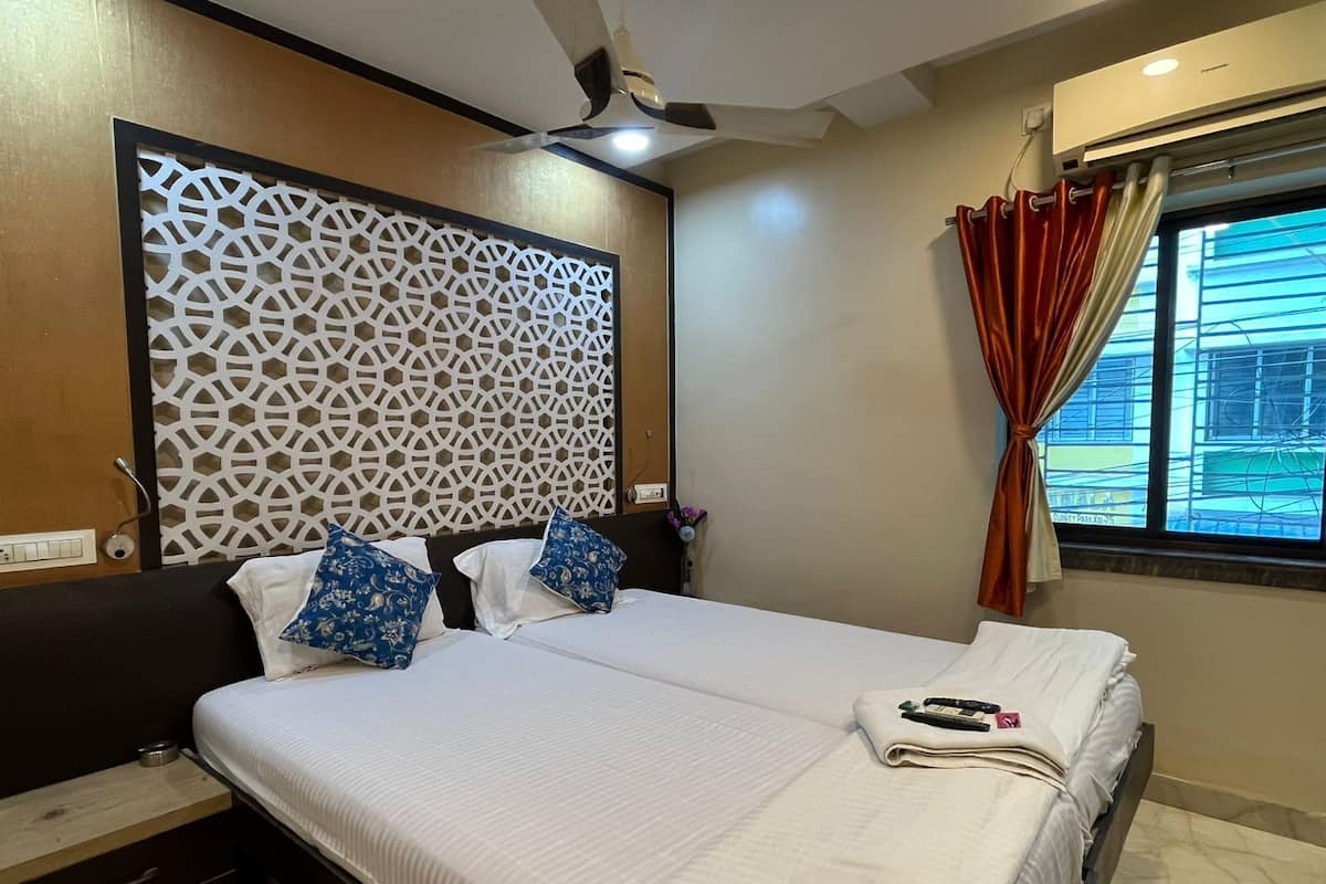 A hotel room with two beds, a decorative wall panel, a ceiling fan, a window with curtains, and a view of buildings outside.