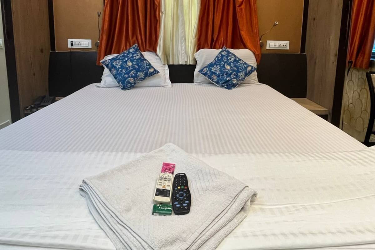 A neatly made bed with a white comforter and two pillows, a remote control, and a card on a folded towel.