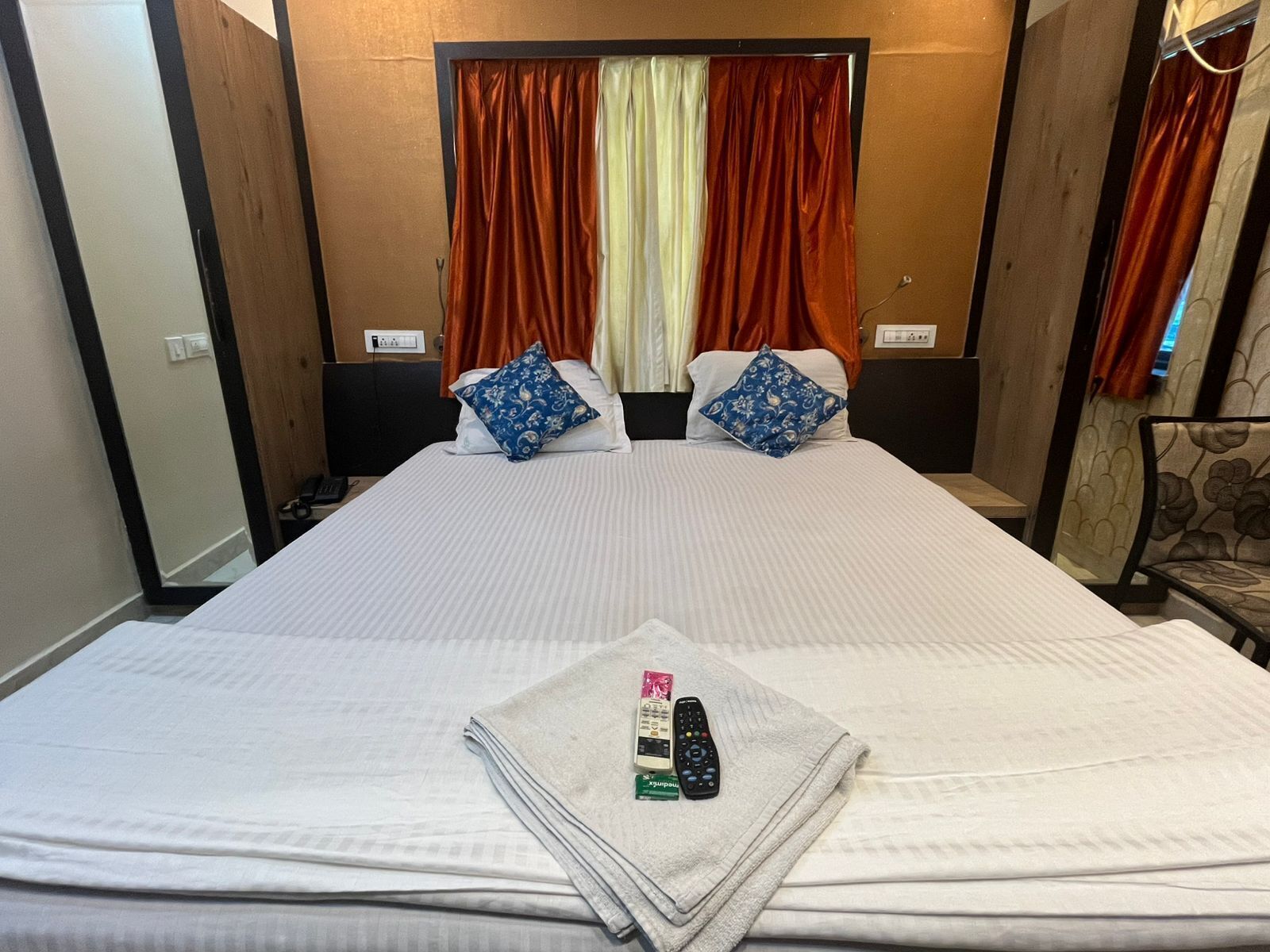 A hotel room with a large bed, two pillows, a remote control, and a folded towel on the bed.