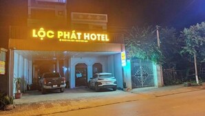 A hotel named Lôc Phát Hotel with a neon sign, a gated entrance, and two parked cars in front. - Loc Phat Hotel MC - by BAY LUXURY (Moc Son)