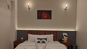A hotel room with a bed, two bedside tables, a nightstand, a wall-mounted picture, and a wall-mounted light fixture. - Sylhet Paradise Inn (Sylhet)
