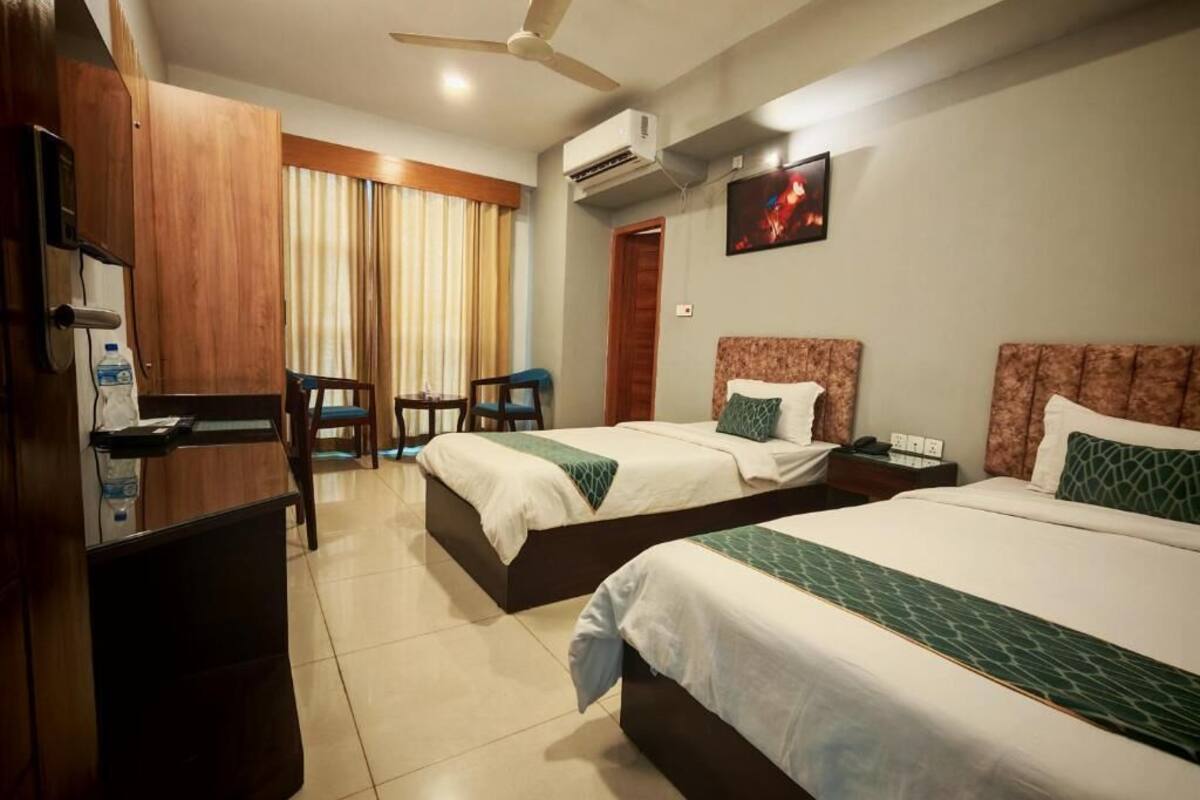 Une chambre d’hôtel avec deux lits, un bureau, une chaise, un climatiseur et un téléviseur.