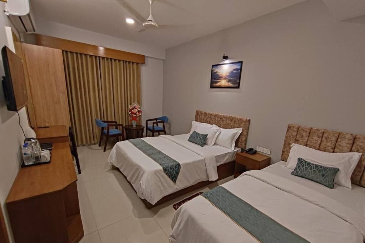 Une chambre d’hôtel avec deux lits, un bureau, une chaise, une télévision et un tableau au mur.