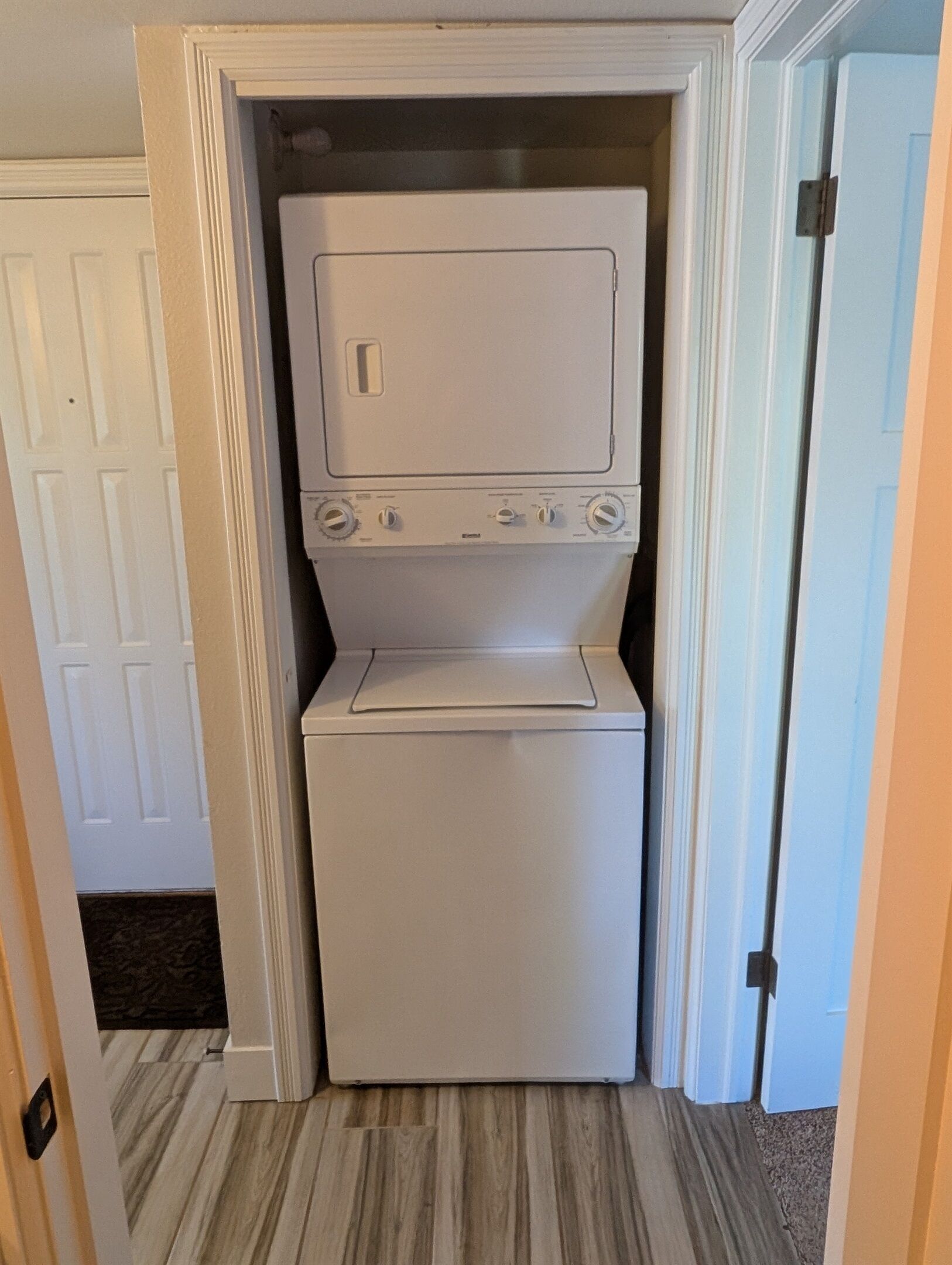 A compact laundry room with a front-loading washer and dryer, a small countertop, and a door leading to another room.