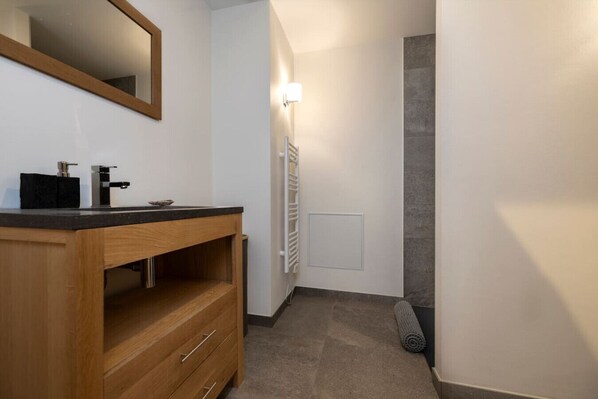 A bathroom with a wooden vanity, a mirror, a towel rack, and a shower area.