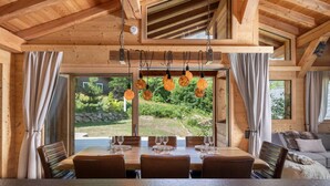 Comedor de madera con una mesa dispuesta para seis personas, ventanas amplias y lámparas colgantes esféricas.
