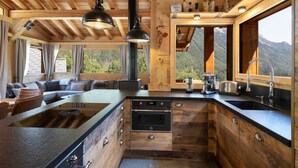 Una cocina moderna con una isla central, horno empotrado y un amplio ventanal con vistas a la montaña.