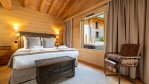 Un dormitorio de cabaña de madera con una cama, una mesita de noche de madera, una silla y una ventana con cortinas.