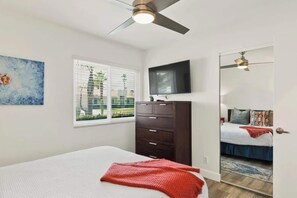 A bedroom with a bed, a dresser, a television, a ceiling fan, a window with blinds, and a painting. - Saltwater Pool & Spa, Fire Pit, Expansive Mountain View (Palm Springs)
