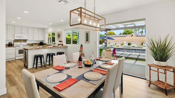 Une cuisine moderne avec des meubles blancs, un coin repas doté d’une table en bois pour six personnes, et une vue sur une piscine extérieure.
