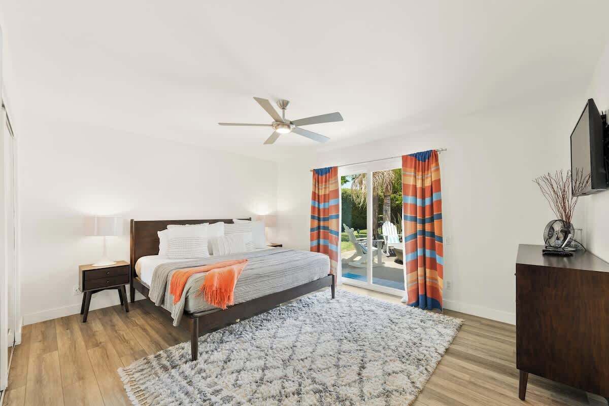 A bedroom with a bed, a ceiling fan, a nightstand, a dresser, and a sliding glass door leading to an outdoor area.