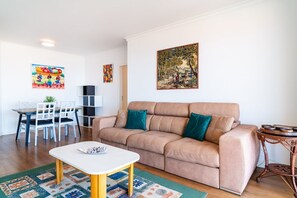A living room with a beige sofa, a white coffee table, and a dining area with a white table and chairs. - GuestReady - Caniço city view (Caniço)