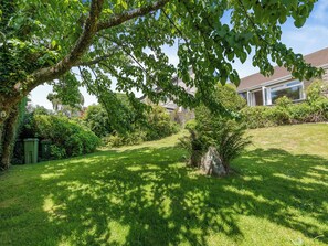 A well-maintained garden with a large tree, a lawn, and a house in the background.