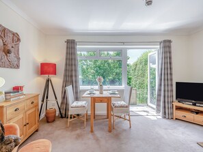 A cozy living room with a dining table, chairs, a TV, and a large window with curtains.