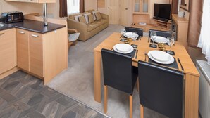 Une chambre d’hôtel compacte comprenant un coin cuisine, un espace repas avec une table dressée pour deux personnes, un canapé et un téléviseur.