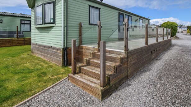 Une maison mobile de plain-pied, dotée d’un porche, d’un petit escalier et d’une allée en gravier.