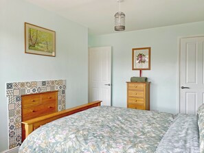 Une chambre à coucher avec une couvre-lit à motifs floraux, une commode en bois, un tableau encadré et un luminaire suspendu.