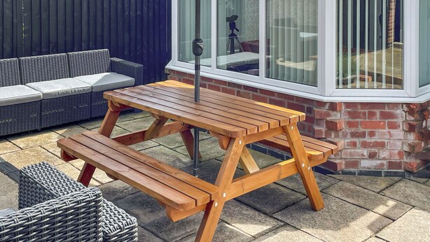 A wooden picnic table with a bench, a wicker sofa, and a window with blinds. - 2 bedroom accommodation in Bottesford (Bottesford)
