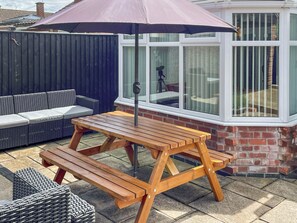 A wooden picnic table with a bench, a wicker sofa, and a window with blinds. - 2 bedroom accommodation in Bottesford (Bottesford)
