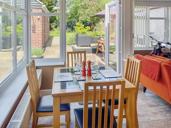 A conservatory with a dining table set for two, chairs, and a view of the garden.