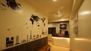 A reception area with a world map mural, a reception desk, a ceiling fan, and a bench. - Hotel Ellora Park (Pune)