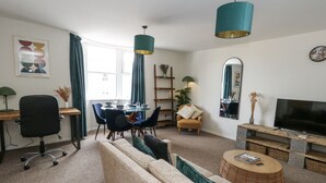 A modern living room with a sofa, chairs, a dining table, and a TV. - Beachcomb (Weymouth)