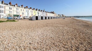 A pebble beach with colorful terraced houses along the shore. - Beachcomb (Weymouth)