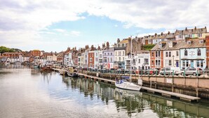 A waterfront with colorful buildings, a dock, and a boat. - Beachcomb (Weymouth)