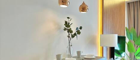 Un comedor moderno con barra, dos lámparas colgantes, un jarrón con plantas y un televisor de pantalla plana sobre un mueble bajo.
