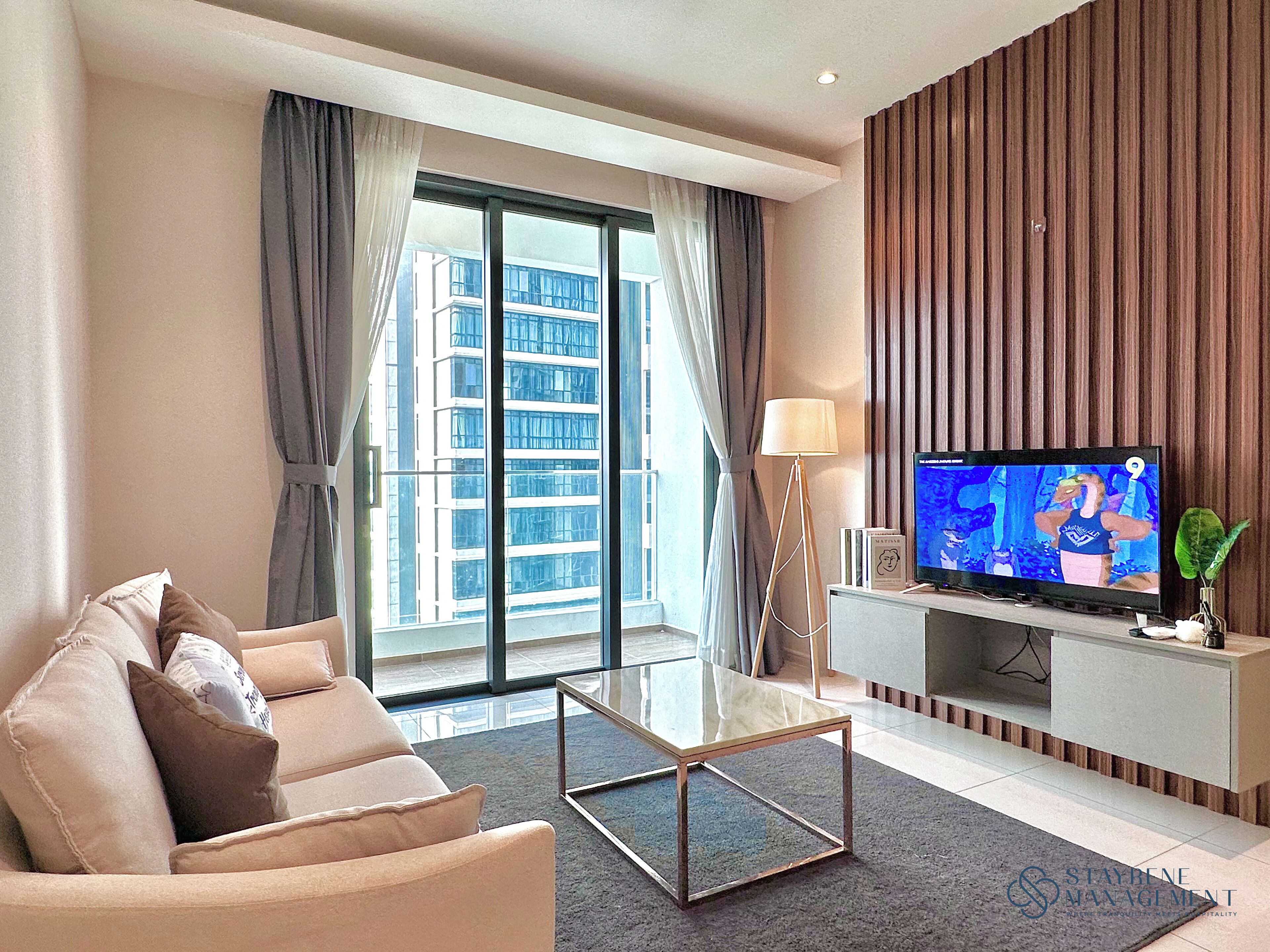 A modern living room with a sofa, a glass coffee table, a TV on a stand, and a large window with curtains.