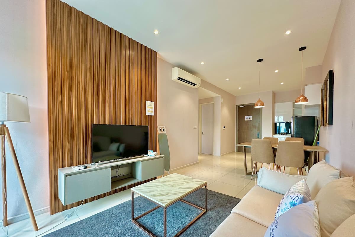 A modern living room with a flat-screen TV, a wooden accent wall, a dining area with chairs, and a sofa with decorative pillows.