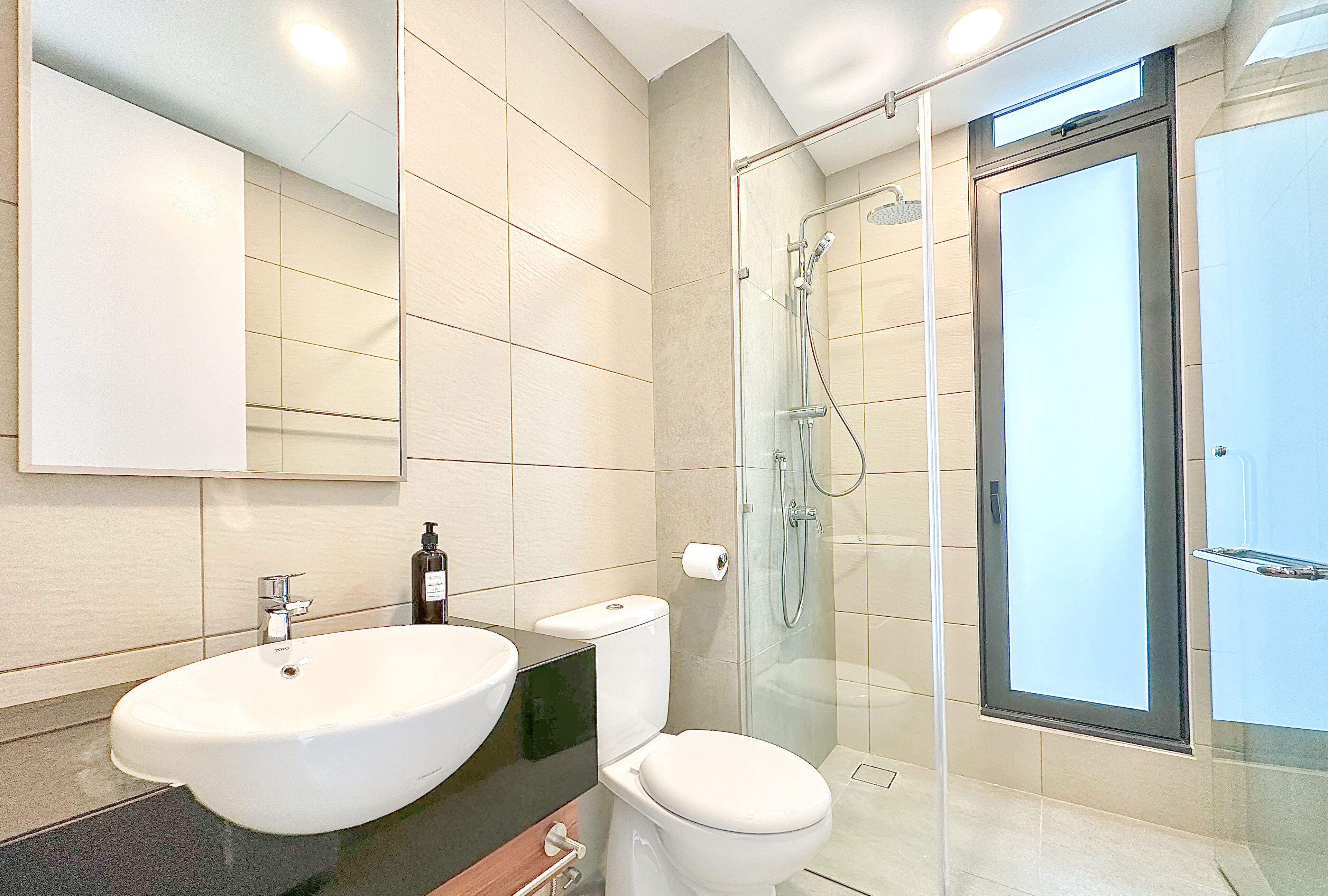 A modern bathroom with a large white sink, a toilet, and a glass-enclosed shower area.